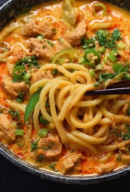 Bowl of Thai-inspired coconut red curry chicken udon with fresh vegetables and herbs